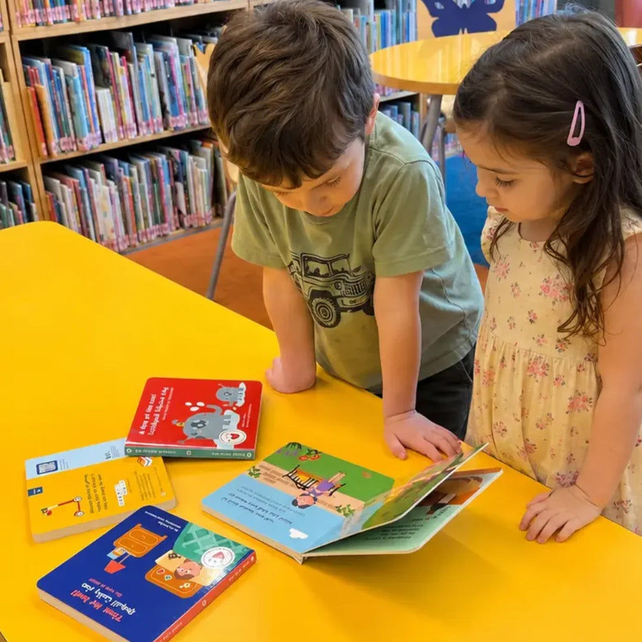 Two young children reading Targhil bilingual Lebanese-English board books at a library table surrounded by bookshelves